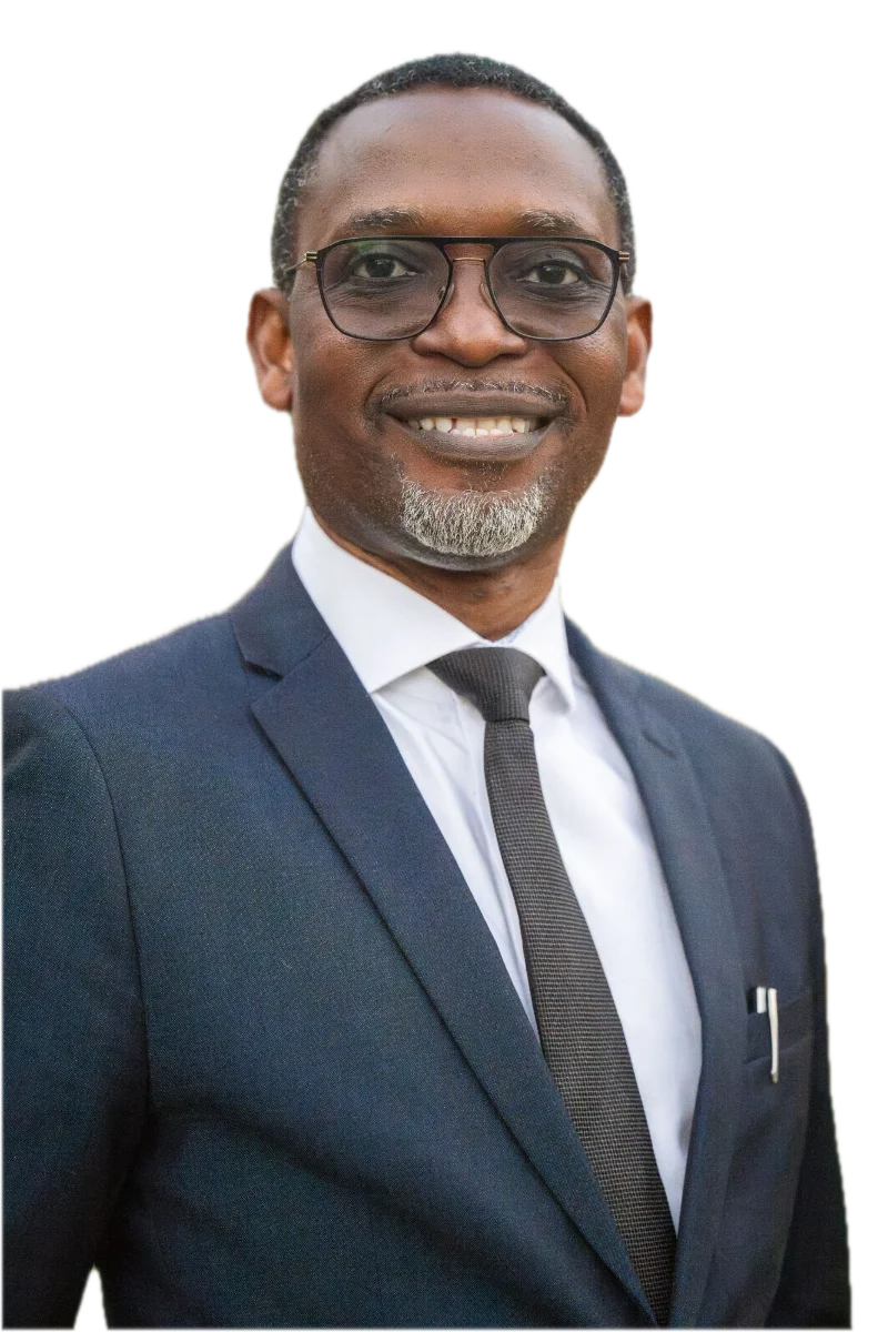 Dr Michaels Aibangbee, smiling, in a navy suit, white shirt and dark tie