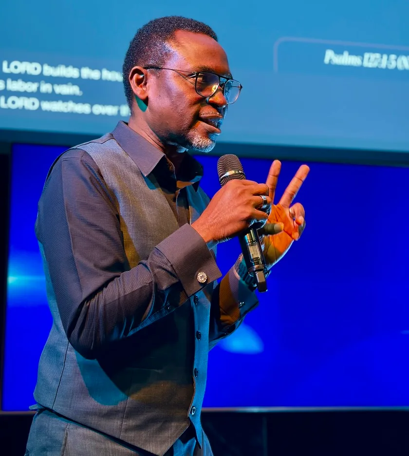 Dr Michaels Aibangbee preaching with a microphone, a psalm on the screen behind him